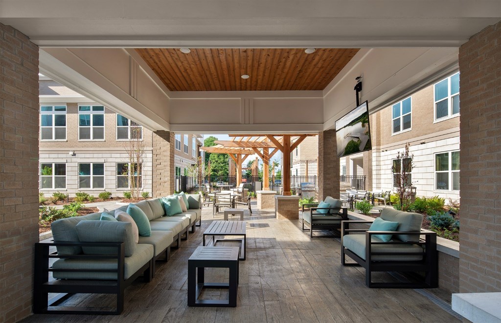 A patio with a long couch and chairs is surrounded by a brick wall.