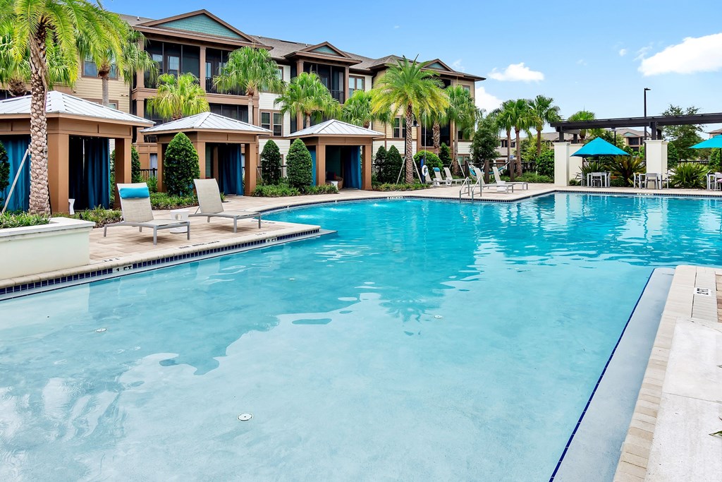 a large swimming pool with lounge chairs and umbrellas in front of a building