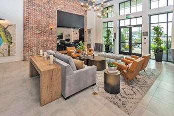 Modern club lounge with floor to high ceiling windows, seating, brick wall, and hanging chandelier - Photo Gallery 2
