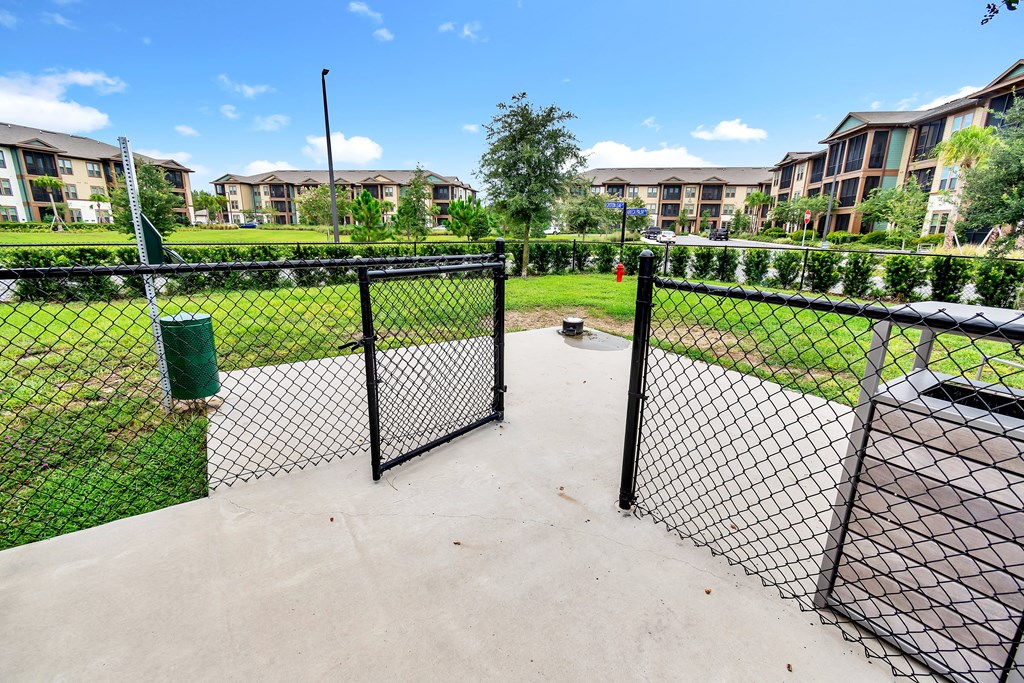 a fenced in dog park with trash cans and apartment buildings in the background