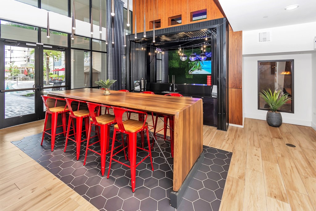 a long wooden table with red chairs in front of a window