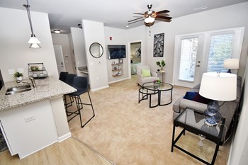 Living room with a ceiling fan with views of the kitchen, entry, and double doors to the patio - Photo Gallery 5