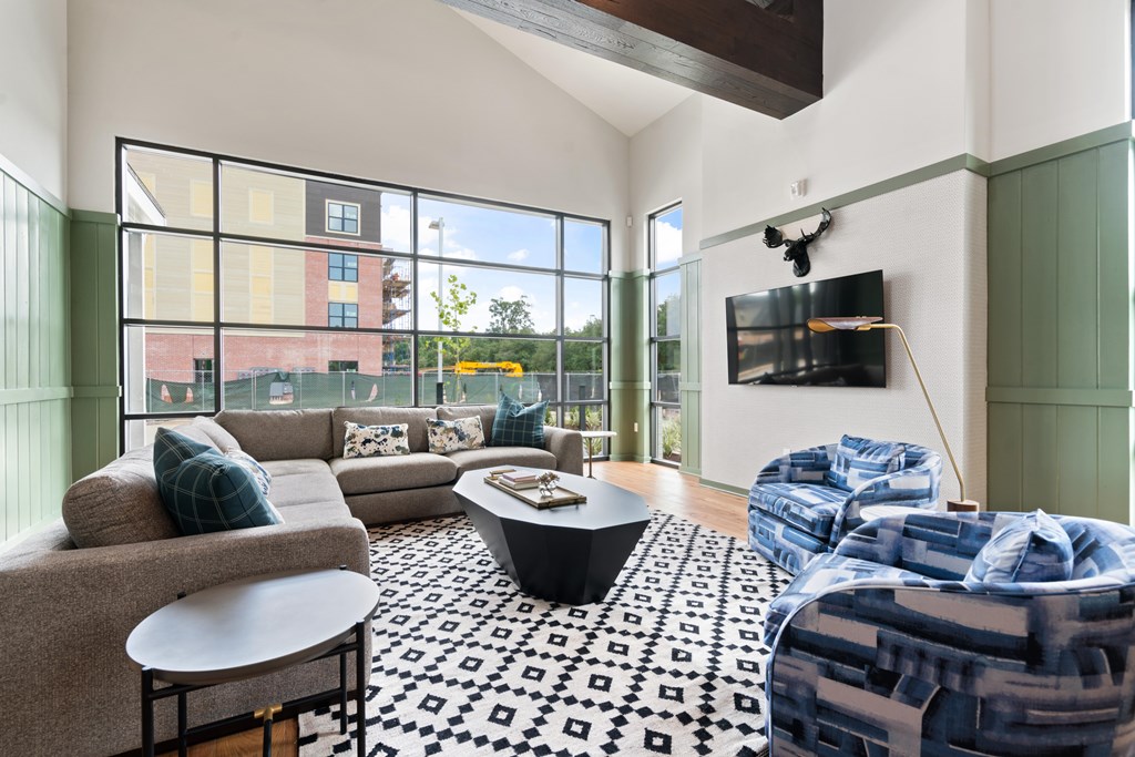 A club room with a black and white patterned rug, a grey couch, a coffee table, and a TV mounted on the wall.