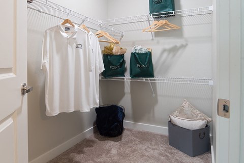 a walk in closet with a white shirt and clothes rack and bags on the wall