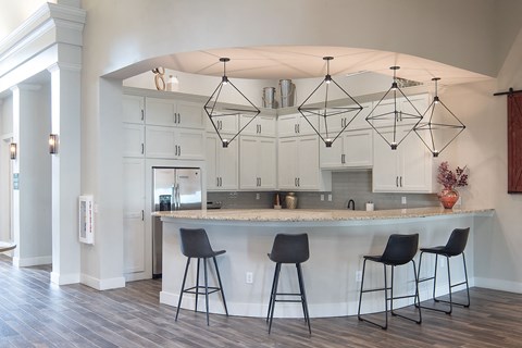 a clubhouse kitchen with a counter top and three bar stools