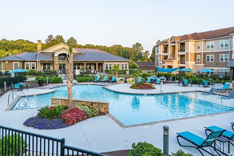 an outdoor swimming pool with chairs and umbrellas in front of an apartment complex