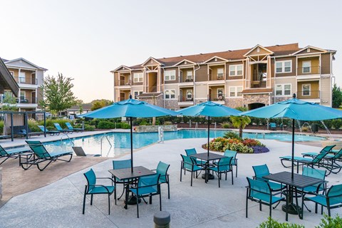 an outdoor pool with tables and umbrellas with apartments in the background