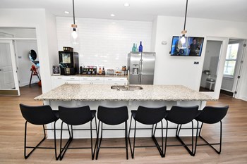 Community kitchen with pendant lights, a large island, stools, a coffee station, and a refrigerator - Photo Gallery 3