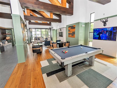 Community room with billiards table, tables with chairs, and a lounge with wooden beams above