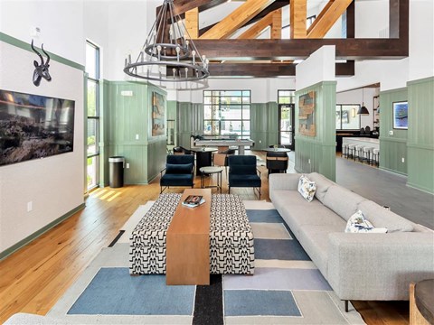 Modern clubhouse lounge with a TV and chandellier, near billiards with a view of a community workspace