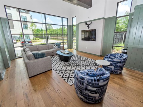 Community room with large windows, an L-shaped sofa, hard floors, chairs, and a TV