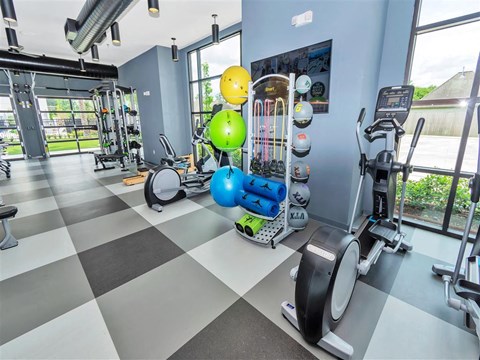 Gym with exercise balls, weights, cardio and weight machines, and glass roll-up doors