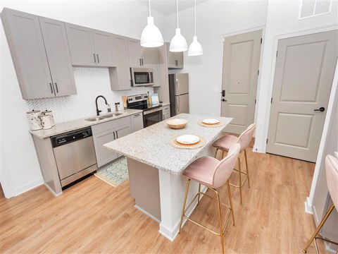 Kitchen with grey cabinets, stainless steel appliances, island with bar seating, and entrance view