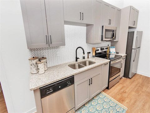 Kitchen with stainless steel appliances, tile backsplash, grey cabinets, and hard floors