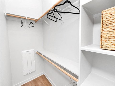 Walk-in closet with built-in shelving, three clothes rods, a fuse box, hangers, and a basket