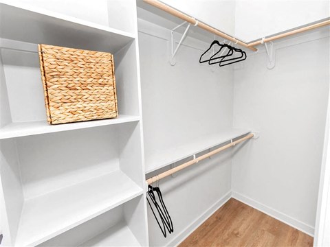 Walk-in closet with hard floors, vertical built-in shelves, and three clothes rods