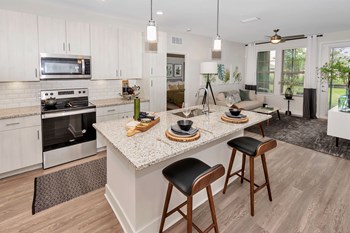 Kitchen with island and barstools looking into living room with windows and doorway to bedroom - Photo Gallery 3