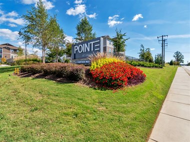 Outdoor Pointe at Greenville entrance sign with bushes, trees, grass, and the sidewalk by the street