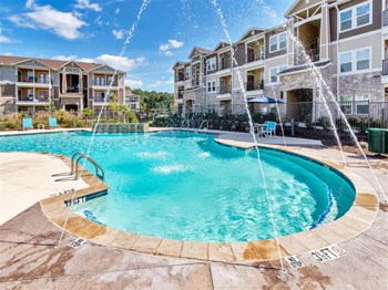Small palm tree island cluster in front of the pool with fountains and apartments in the back - Photo Gallery 2