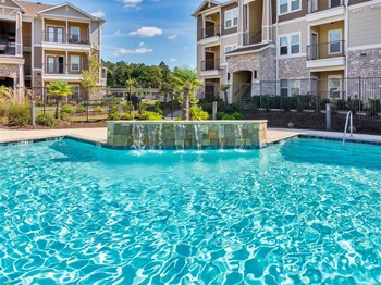 Water fountain splashing into the pool with chairs, trees, and apartments in the back - Photo Gallery 3
