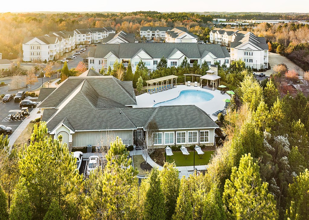 A large clubhouse building with a pool surrounded by trees.
