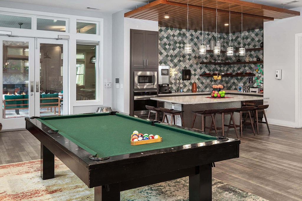 a pool table in a clubhouse with a bar and a kitchen
