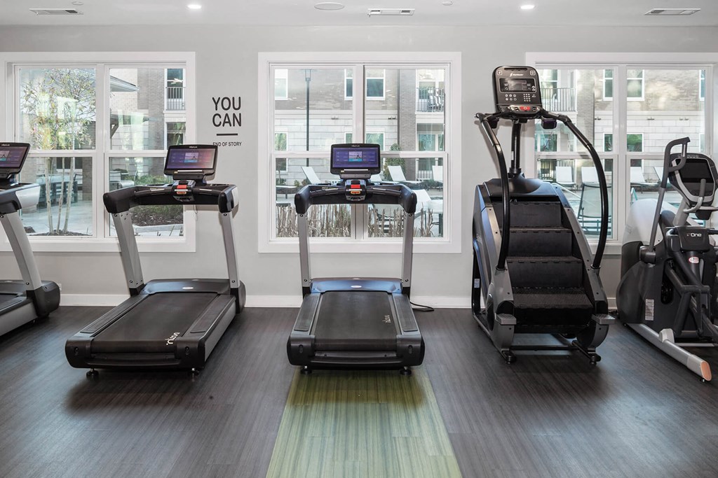a gym with cardio equipment and large windows