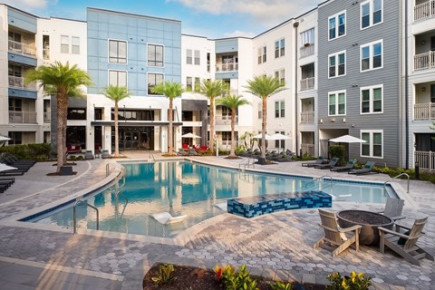A swimming pool surrounded by chairs and palm trees in front of apartment buildings.