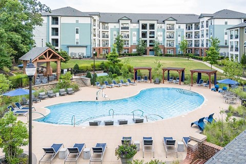 an outdoor pool with chairs around it and an apartment building at TRAILSIDE VERDAE APARTMENTS, GREENVILLE, South Carolina