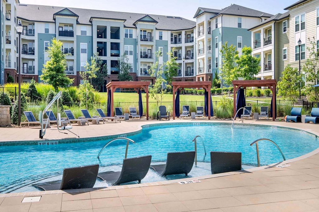 an outdoor pool with chairs and an apartment building in the background