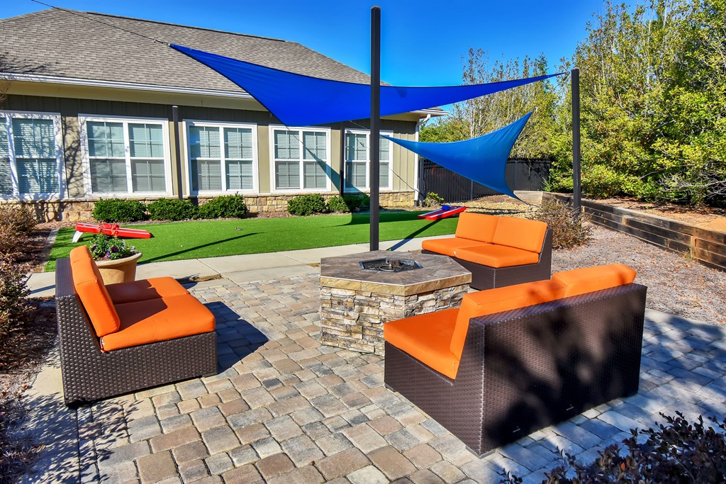 a patio with a fire pit and lounge chairs in front of a house