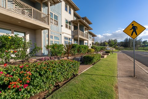 A pedestrian crossing sign is on the side of a road in front of a building with a well-maintained garden.