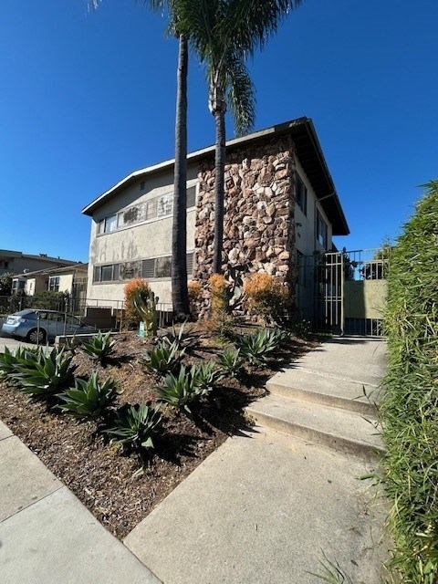 A house with a stone wall and a palm tree in front.