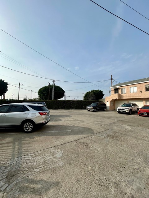 A silver car is parked in a lot with other cars and a house in the background.