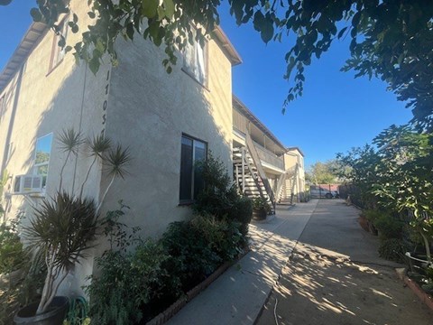 A sunny day in a quiet residential street with a house on the left and a tree in the foreground.