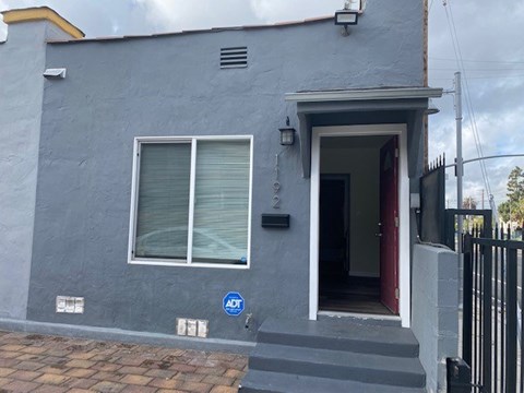 A grey house with a red door and a blue sign on the front.