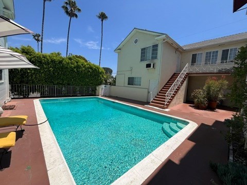 A pool in a backyard with a house and palm trees in the background.