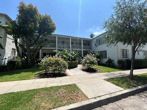 A sunny day at a white building with trees and bushes in front.