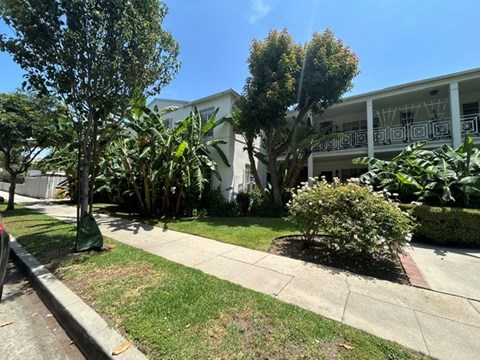 A white building with a balcony is surrounded by greenery.