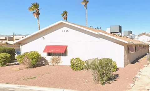 A white building with a red awning is surrounded by palm trees.