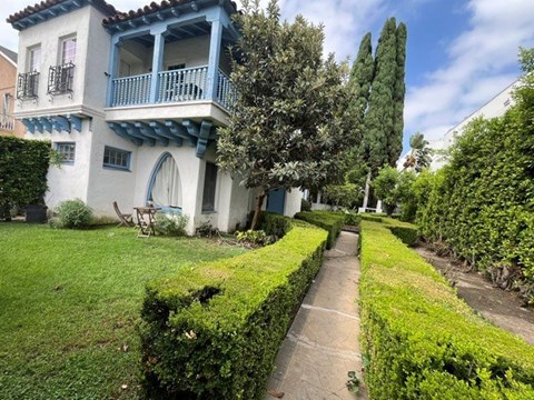 A white and blue house with a balcony and a hedge in the front yard.