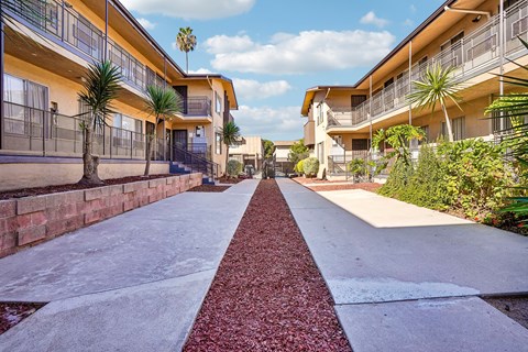 A long, narrow walkway with a red brick border separates two rows of apartment buildings.