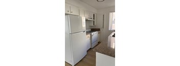 A white refrigerator is in a kitchen with white cabinets.