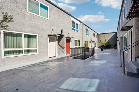 A long, narrow courtyard between two buildings with a black metal fence and a green mat on the ground.