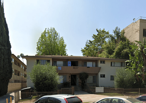 A building with the number 837 on it is surrounded by trees and has cars parked in front.