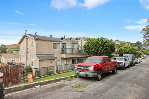 A red pickup truck is parked on the side of a street lined with houses and parked cars.