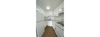 A white kitchen with a refrigerator, stove, and sink.