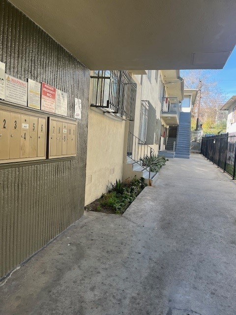 A long concrete walkway leads to a building with a row of mailboxes on the left.