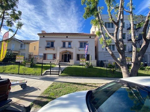 A white car is parked in front of a building with a black fence.