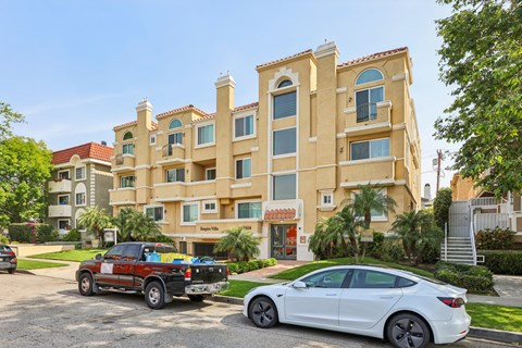 A white car is parked in front of a building with a red truck parked behind it.